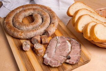Sliced roasted traditional homemade sausage with spices and herbs. Baked pork with herbs and spice on wooden board and and slices white wheat bread.