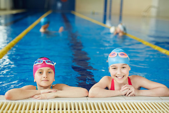 Portrait of two schoolgirls smiling and looking at camera at pool swimming practice
