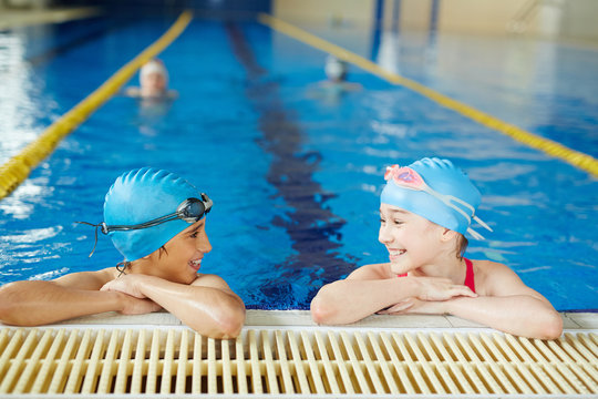 Two children wearing caps and goggles laughing and having fun at PE lesson in clear water of swimming pool