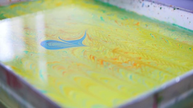 Liquid Ebru art technics - drawing brush create a picture on water - blue circle on yellow background