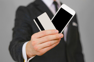 Businessman showing closeup of white smartphone with blank black screen and a credit card. Phone and card hold hands. Show clear telephone. Man in a black suit, white shirt and tie