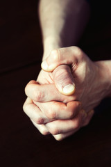 Man's strong hands clasped on dark wooden table.