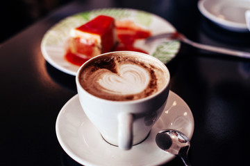 cup of coffee cappuccino art and cheesecake on the table in a cafe
