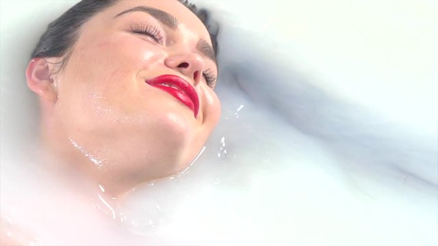 Beautiful fashion model girl in milk bath. Spa and skin care concept. Beauty sexy woman  relaxing in milk bath. 4K, slow motion UHD video