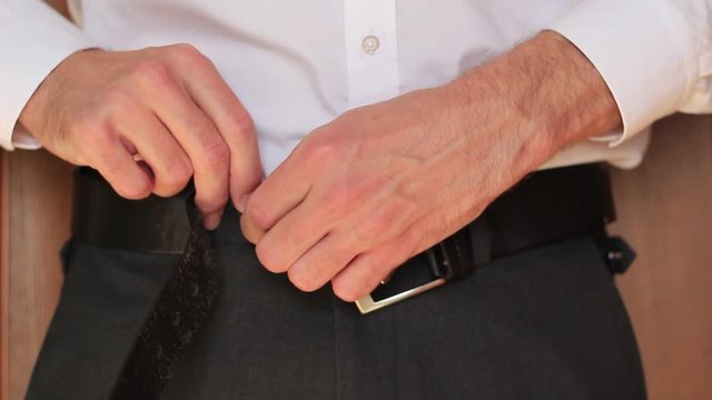 Businessman putting his trousers on and tightening a belt