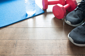 Sport equipments on wooden floor, red dumbbells, sneaker and bottle of water on yoga mat