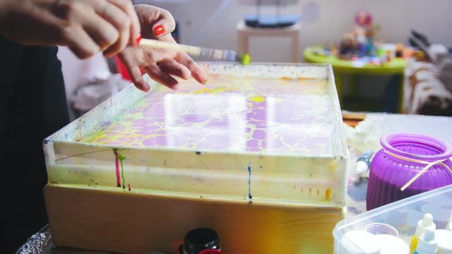 Process of painting - yellow paint drops on the purple circles - woman draws on water in Liquid Ebru art technics