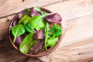 Mixed salad leaves on wooden rustic background with top view. Healthy food, healthy lifestyle and diet concept. Fresh green salad with spinach, arugula, chard leaves, lettuce. Copy space