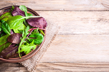 Mixed salad leaves on wooden rustic background with top view. Healthy food, healthy lifestyle and diet concept. Fresh green salad with spinach, arugula, chard leaves, lettuce. Copy space