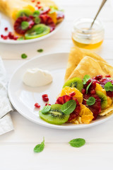 Thin crepes with fresh kiwi, orange, sicilian orange, honey, cream and mint leaves on white rustic wooden table. Selective focus