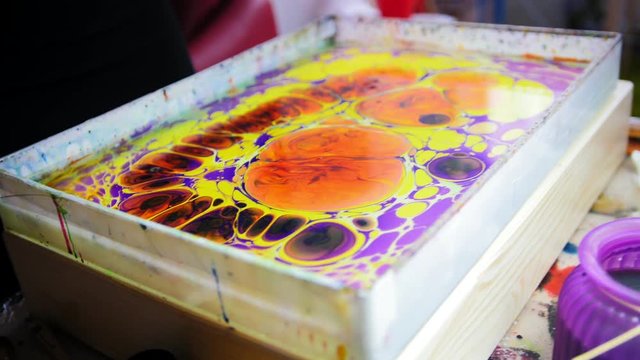 Process of painting - dripping colorful paint - woman draws on water in Liquid Ebru art technics