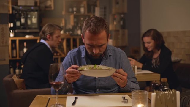 Middle-aged Caucasian male with light bristle and jeans shirt looking at plate with salad with suspicion and then asking why at camera in slowmotion