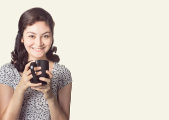 happy smiling woman in casual clothes holding white cup of coffee or hot beverage on plain background, room for copyspace