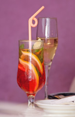 two glass transparent wine glass with a cocktail and champagne on a pink background