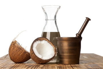 open coconut, brass crushing mortar and a bowl of coconut oil on a wooden board