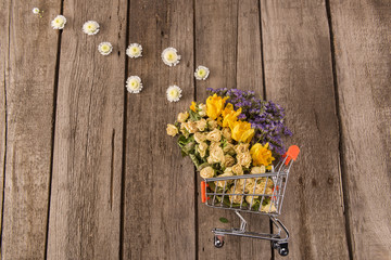 Spring floral composition with Beautiful various spring flowers in small shopping trolley on wooden table