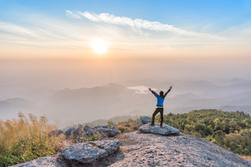 Man successful climbing spreading hand on the cliff and enjoy sunrise view.