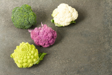 Fresh organic white and purple cauliflower, broccoli, romanesco. On gray background, bowl, wooden cutting board.