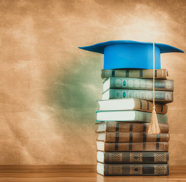 Graduation mortarboard on top of stack of books on abstract background of wall