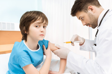 doctor in medical uniform making injection to upset boy patient in bed