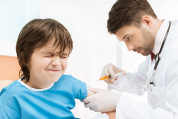 side view of doctor making injection to boy patient in bed