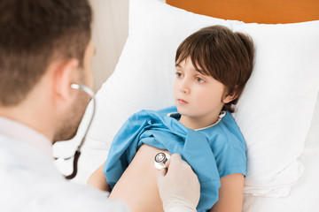side view of doctor in gloves examining little boy with stethoscope