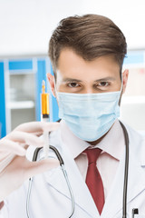 portrait of serious doctor in mask holding syringe in lab