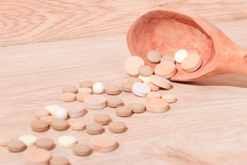 Fototapeta na wymiar Close-up shooting of wooden spoon and colorful pills isolated on wooden background