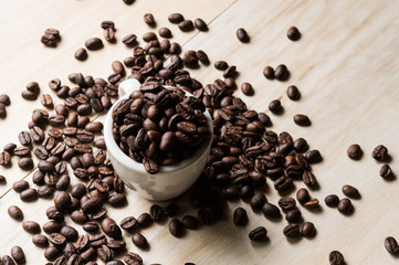Cup full of coffee beans on wood background