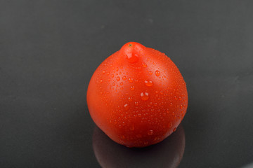 Single red tomato with drops isolated on black background. Juicy organic cherry perfect for salads, soups, sandwiches or healthy snack.