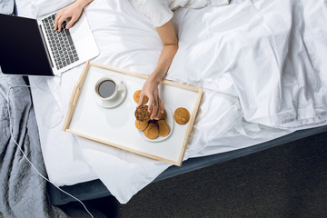 top view of woman using laptop and eating breakfast in bed