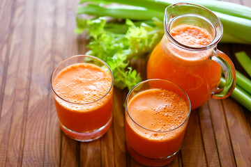 Fresh carrot juice poured into glasses and green celery