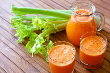 Fresh carrot juice poured into glasses and green celery