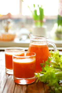 Fresh carrot juice poured into glasses and green celery