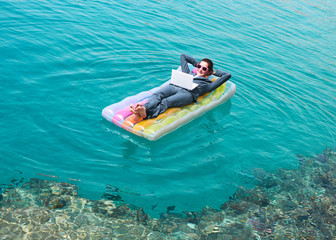Happy businesswoman floating with laptop on lilo