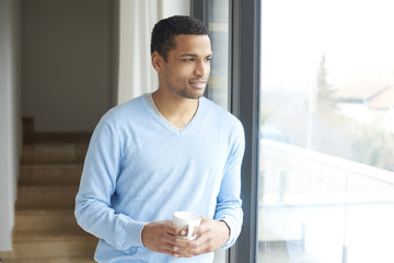 Confident young man portrait. Shot of a young man relaxing by the window at his modern home with a cup of tea.  