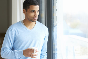 Confident young man portrait. Shot of a young man relaxing by the window at his modern home with a cup of tea.  