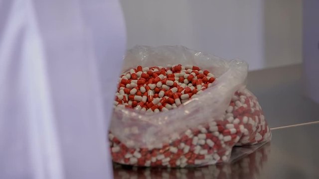 A woman in a white gown is grabbing a small shovel with red-and-white pills and is putting them in a big funnel.

