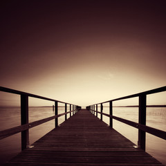 Fototapeta na wymiar Long Wooden Pier into a Lake, perfect symmetry, black and white, sepia toned