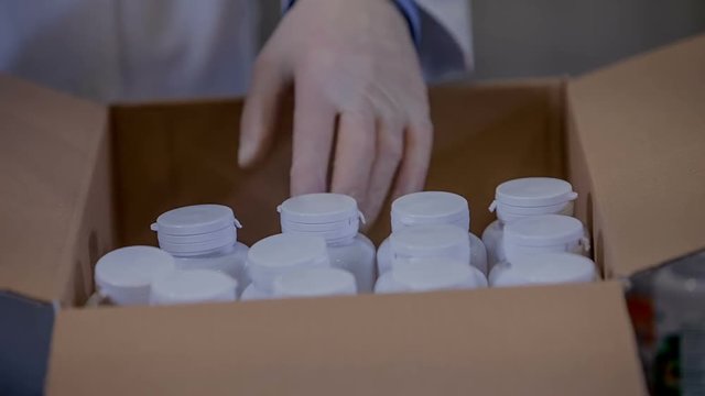 A worker in a factory is organizing white cups in a big box. The cups have lots of different sorts of pills in them.
