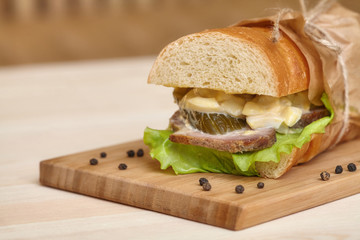 Big sub sandwich baguette with ham on wooden cutting board
