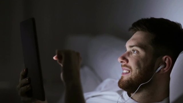 man with tablet pc and earphones in bed at night