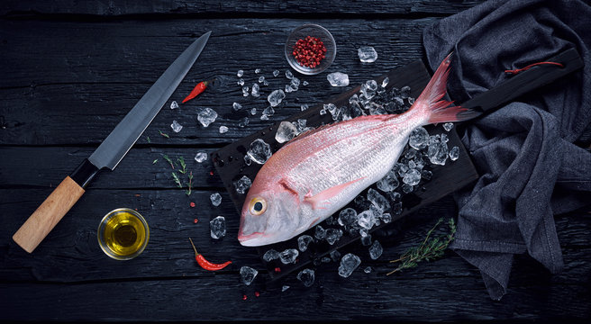 Fresh spanish bream fish (breca) on ice on a black wooden table top view
