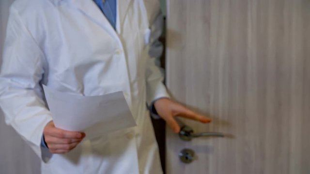 A pharmaceutical worker is coming through one door and is closing them. Then he opens another door and goes through. He is holding a piece of paper in his hand.
