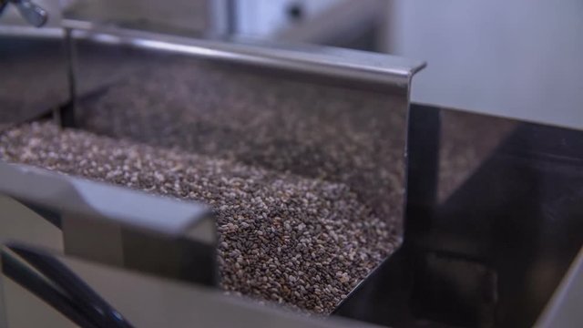 Someone is turning on a machine and we can see chia seeds moving and falling into a big container.
