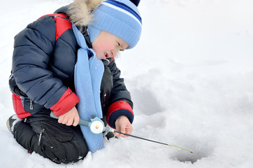 Fototapeta na wymiar Little boy fishing on the frozen river in winter.