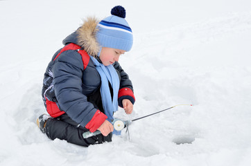 Little boy fishing on the frozen river in winter.