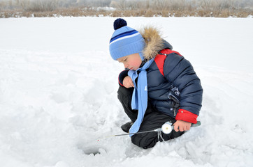 Fototapeta na wymiar Little boy fishing on the frozen river in winter.