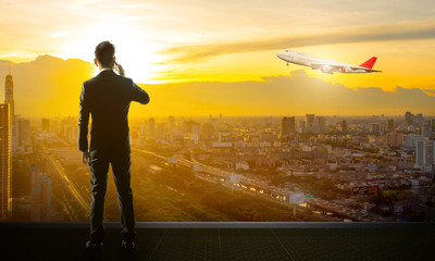 Businessman standing and using his smartphone at terminal airport over sunset cityscape.
