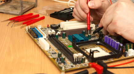 Master is looking for the fault of the motherboard with a multimeter.
